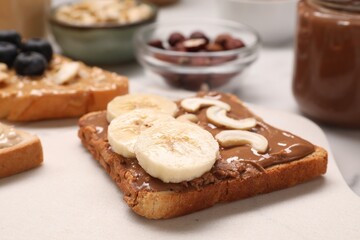 Toast with nut butter, banana slices and cashews on white table, closeup
