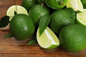Pile of fresh wet limes and leaves on wooden table, closeup