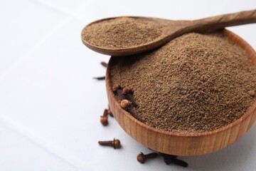 Aromatic clove powder in bowl, dried buds and spoon on white table, closeup. Space for text