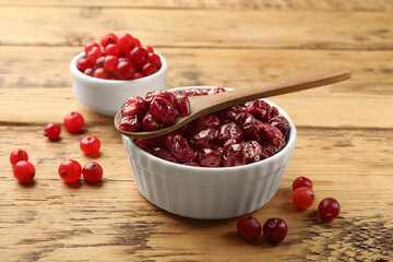 Tasty dried cranberries in bowl and fresh ones on wooden table, closeup