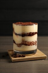 Delicious tiramisu in glass and coffee beans on wooden table