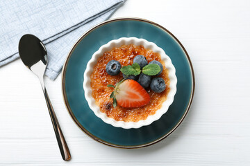Delicious creme brulee with berries and mint in bowl on white wooden table, top view