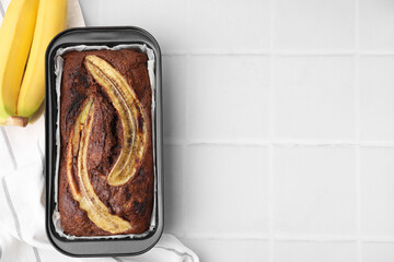 Delicious banana bread and fresh fruits on white tiled table, top view. Space for text