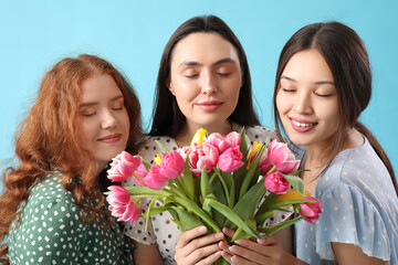 Young women with bouquet of beautiful tulips on blue background. International Women's Day