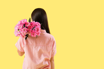 Young woman with bouquet of pink chrysanthemum flowers on yellow background. International Women's Day