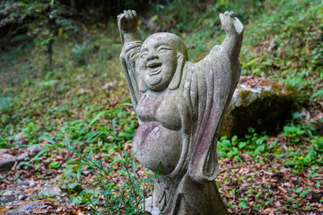 Moss covered stone Buddhist monk carving with arms raised