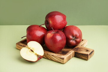 Wooden board with fresh red apples on green background