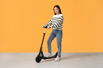 Beautiful young Asian woman with modern electric kick scooter near yellow wall © Pixel-Shot