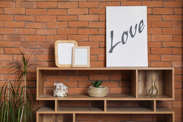 Modern shelving unit with poster and blank frames near brick wall