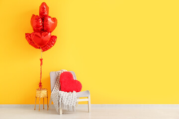 Grey armchair with heart-shaped cushion and balloons near orange wall. Valentine's Day celebration