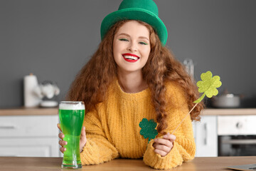 Young woman with beer and paper clover celebrating St. Patrick's Day in kitchen