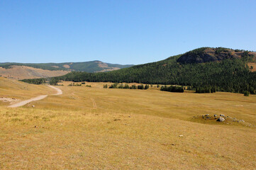 The winding field road goes around the hills through the dry autumn steppe towards the high mountains.