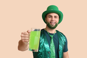 Young man in leprechaun hat with green beard holding glass of beer on beige background. St....