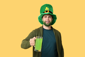 Young man in leprechaun hat with green beard holding glass of beer on yellow background. St....