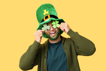 Young man in leprechaun hat with green beard holding clover on yellow background. St. Patrick's Day...