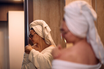 A woman gracefully applies nourishing moisturizer to her shoulder after a relaxing bath, embodying...