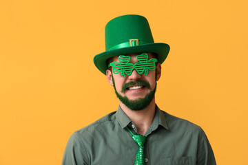 Young man in leprechaun hat and decorative glasses in shape of clover with green beard on yellow...