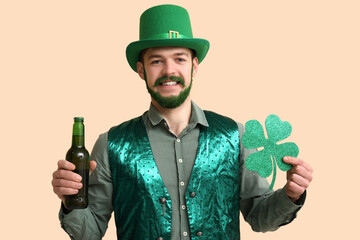 Young man in leprechaun hat with green beard holding bottle of beer and clover on beige background....