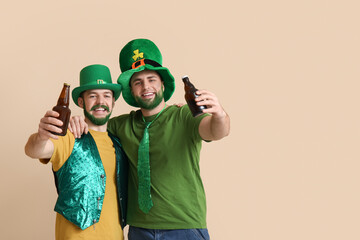 Happy young men in leprechaun hats with green beards holding bottles of beer on beige background. St. Patrick's Day celebration