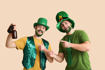 Young men in leprechaun hats with green beards pointing at bottles of beer on beige background. St....
