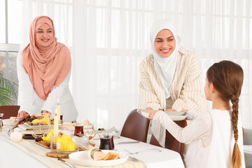 Young Muslim woman with her mother and little daughter setting table at home. Ramadan celebration