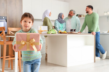 Little Muslim girl with gift and her family in kitchen. Ramadan celebration