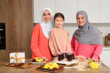 Young Muslim woman with her mother and little daughter celebrating Ramadan at table in kitchen