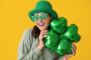 Happy young woman in leprechaun hat and decorative glasses with air balloon in shape of clover on...