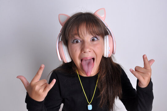 pr&eacute; adolescente mostrando a lingua engra&ccedil;ada  e feliz com fones de ouvido escutando musicas