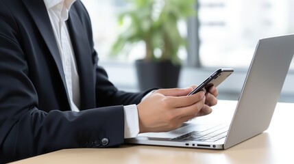 A Close-up of an Asian businesswoman using a mobile phone while working on a laptop computer, white isolated background.