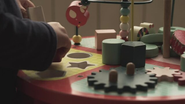 Little kid picking up wooden shapes and putting them in the right holes. Brain develpment educational toys for children. Infant developing new skills.