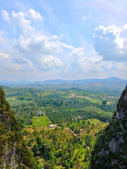 Fototapeta premium Mountain view on a high cliff with nature and green trees surrounding . Aerial view of Beautiful natural scenery mountain. Wallpaper background nature cloud sky. Happy relax holiday 