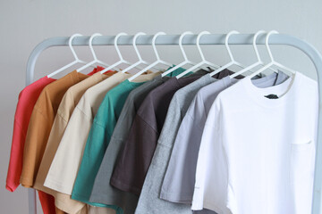 Fototapeta premium Collection of multicolor plain t-shirts hanging on white clothes hanger in closet or clothing rack over white background