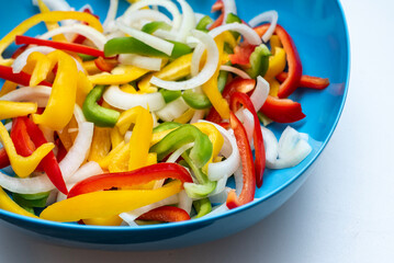 blue bowl of colorful nutritious sliced bell peppers and onions for fajitas 