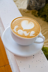 heart-shaped latte art in a white cup on a wooden table.