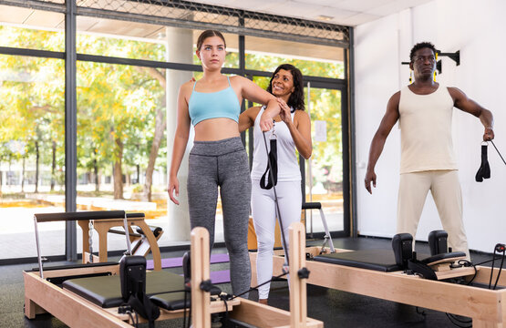 African-american man and young european woman exercising with pilates reformers. Latin woman instructor assisting them with workout.