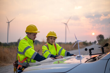 Engineer wearing uniform read blueprint document inspection work in wind turbine farms rotation to electricity,standing in front of car Model windmill and wind force meter is ecology energy concept.