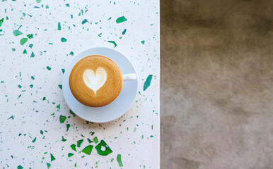 A cappuccino with heart foam art on a terrazzo table, split with a concrete floor - Powered by Adobe