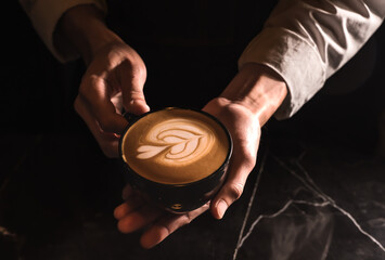 Close up barista hands holding cup of coffee latte art on black background