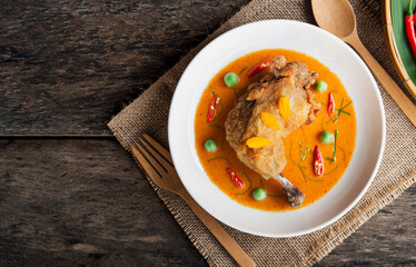 Top view of crispy fried chicken with red curry (Panang Sauce) in white plate on wooden table background. Thai Food