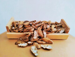 In the picture there are some peanut shells placed in a brown wooden container. The peanut shells are brown and are used to put on trees as fertilizer.