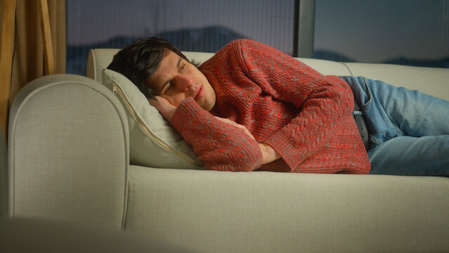 man lays down himself on pillow on the sofa in living room. Male trying to relax after tiring work day at home