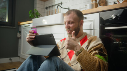 Smiling man entering credit card number on tablet device for makes distant goods purchase, secure...