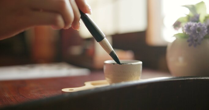 Brush, closeup and hands at a table for calligraphy, writing or ancient Japanese art in a house. Letter, communication and zoom on person fingers with traditional ink stroke, penmanship or art tool