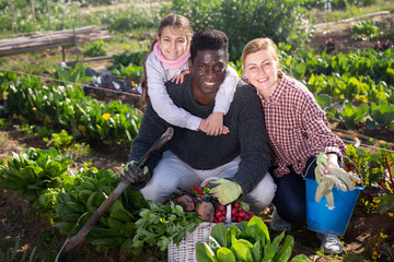 Portrait of happy cheerful couple of farmers with daughter sitting outdoors and smiling at the farm