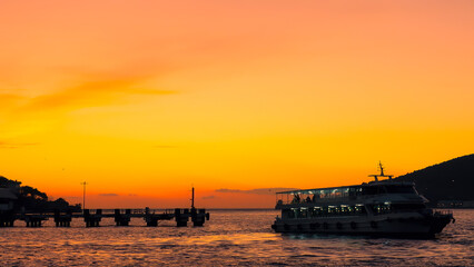 Obraz premium Orange seascape at dawn with silhouettes of passing ferry boat. Turkey