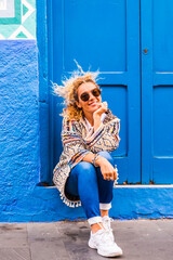 Chererful and relaxed beautiful woman sit down outside a colorful blue house in the street - home properties owner people concept - travel lifestyle and scenic places to discover