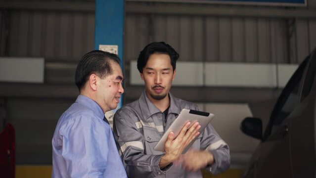 Japanese male mechanic with Asian adult service users Discussing a deal while repairing a car in the auto repair shop, Technician is presenting to customer in the garage