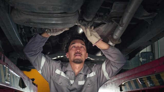 Japanese auto mechanic working underneath car lifting machine at the garage, asian man worker auto repairs in car service