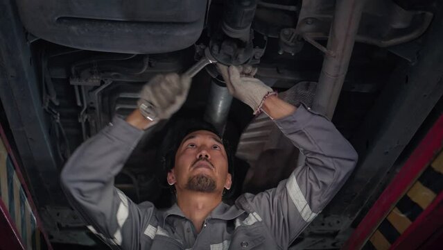 low angle of Japanese auto mechanic working underneath car lifting machine at the garage, asian man worker auto repairs in car service